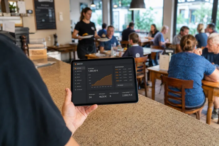 Ein Tablet zeigt die Umsatzkurve, dahinter läuft der Service weiter