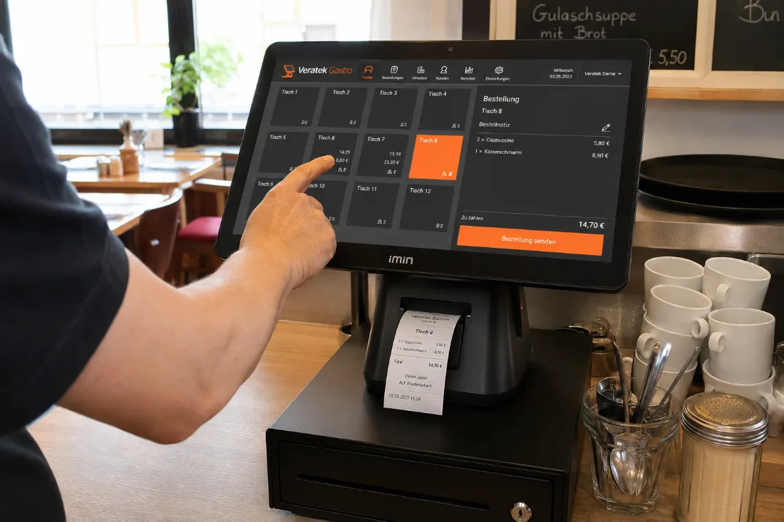 Eine Hand bedient das Kassenterminal am Tresen, daneben liegt der frisch gedruckte Beleg