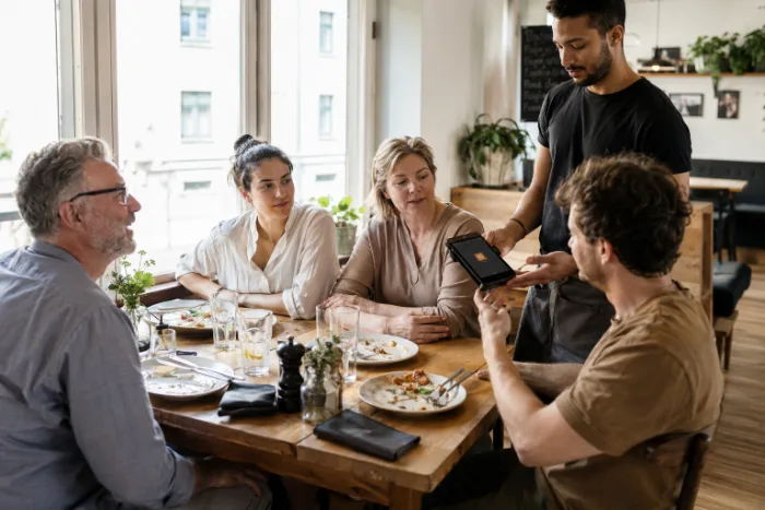 Ein großer Tisch beim Zahlen, die Servicekraft hält das Gerät hin