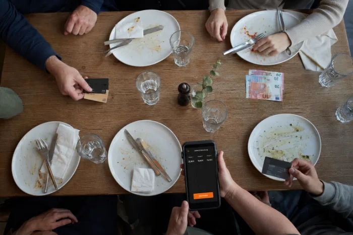 Ein Tisch nach dem Essen von oben: leere Teller, mehrere Karten und Scheine liegen bereit